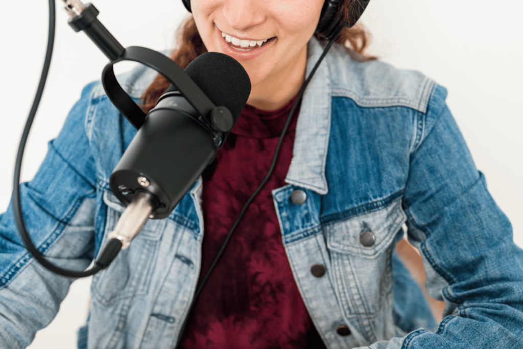 Happy female podcaster speaking into a studio mic while wearing headphones.