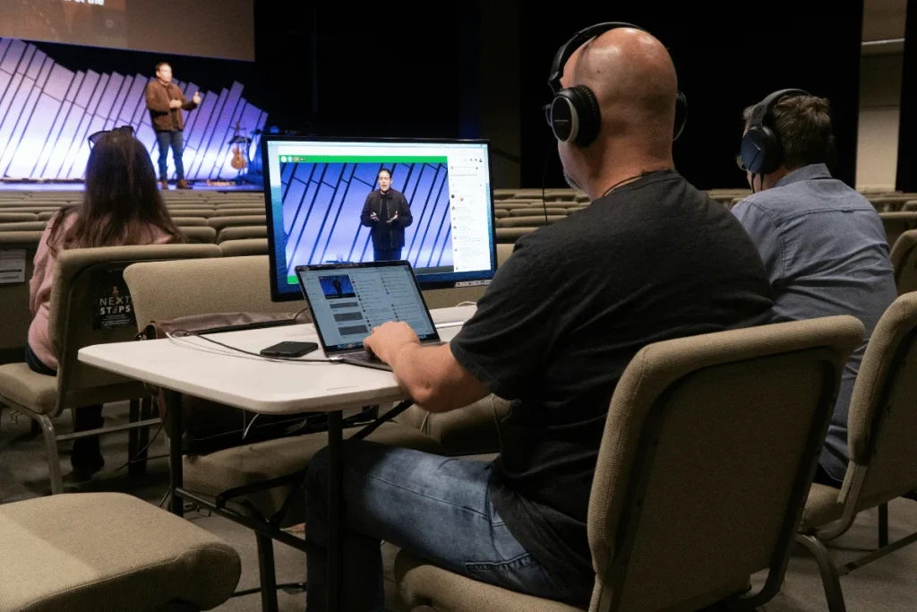 Video crew monitoring a live-streamed presentation in a large auditorium.