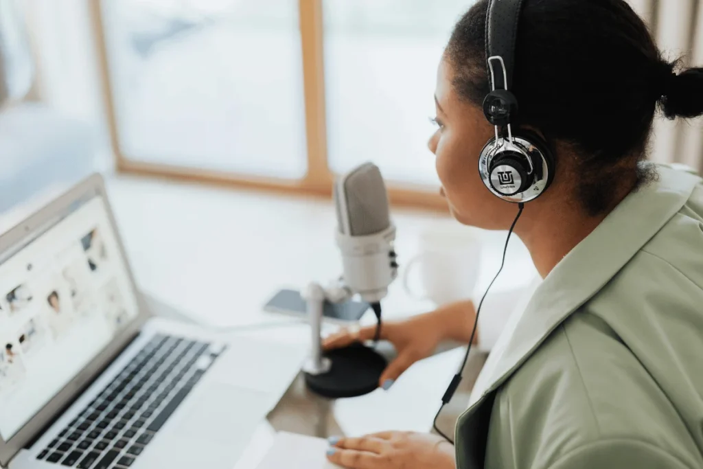 Podcaster wearing headphones, speaking into a microphone while using a laptop.