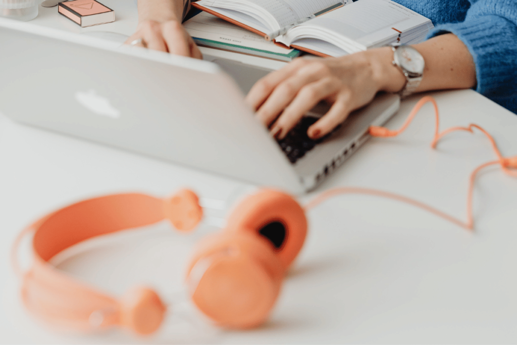 Study setup with laptop, open book, and bright orange headphones.