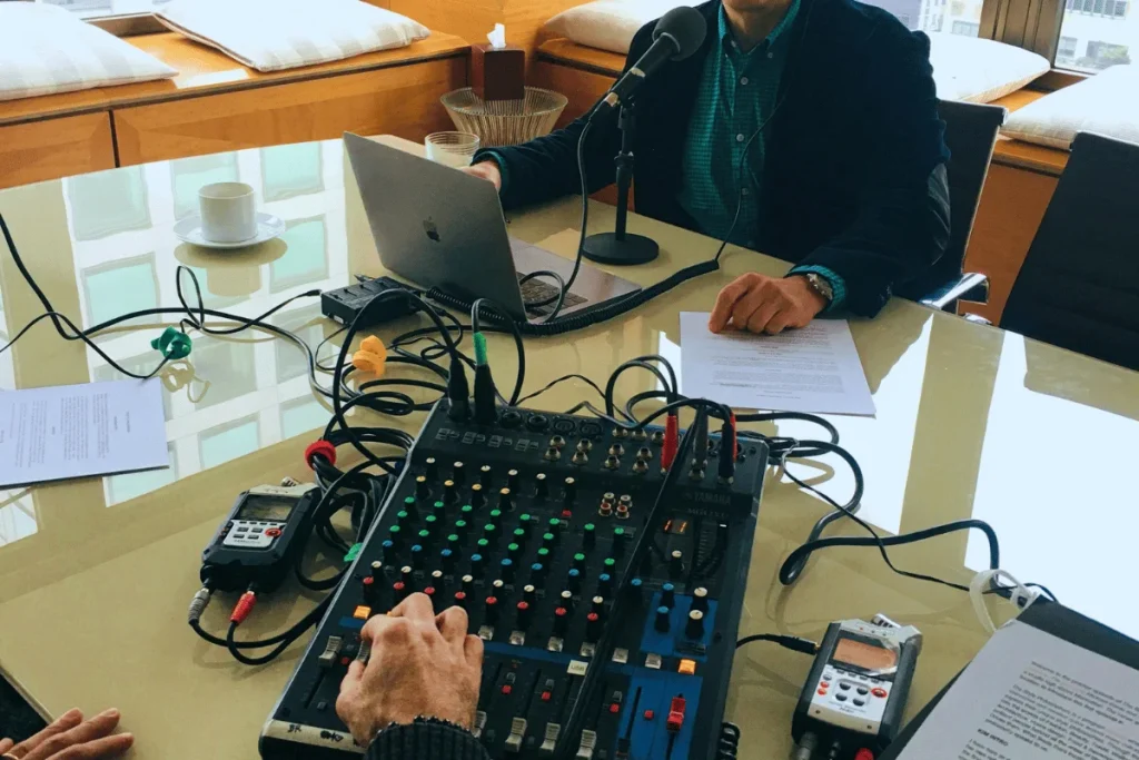 Podcast recording session with a laptop, audio mixer, and microphone set up on a glass table for professional audio production.