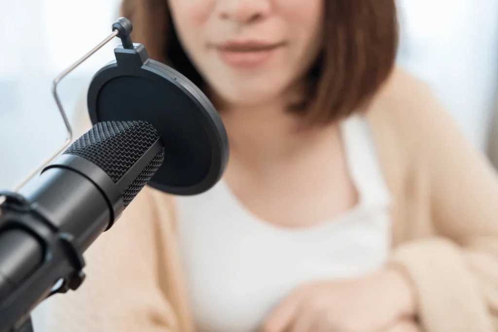 Professional podcasting setup with condenser microphone and pop filter in front of computer screen.