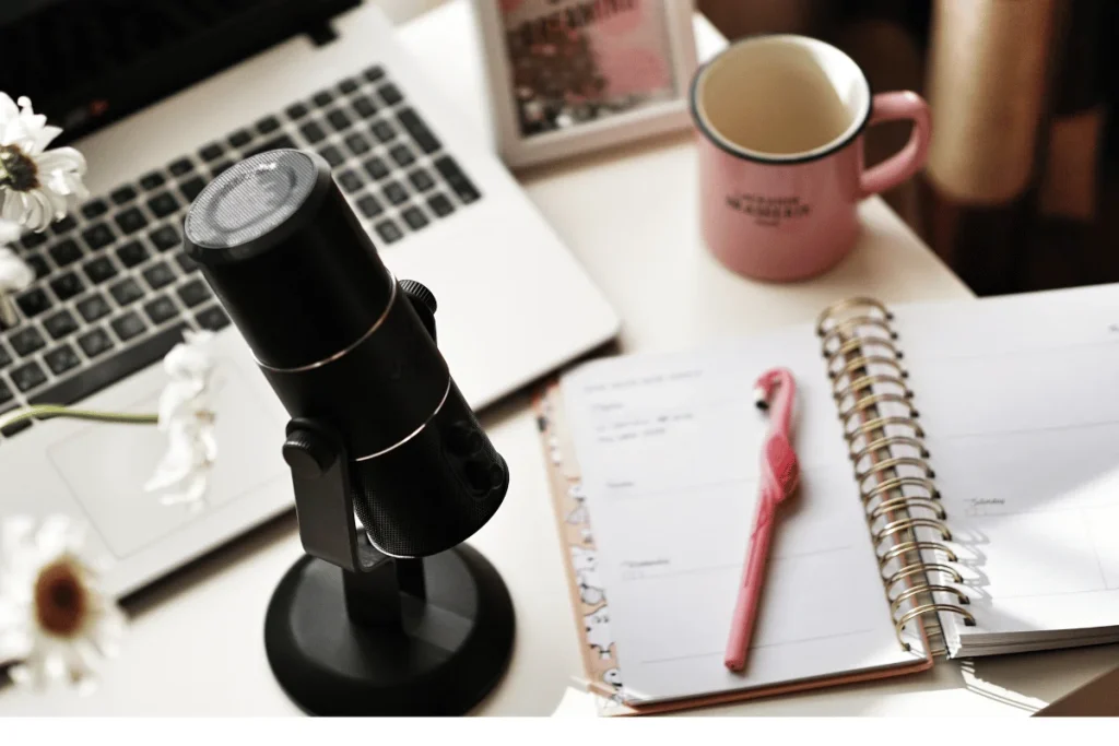 Professional black microphone in front of a laptop, next to a spiral notebook.