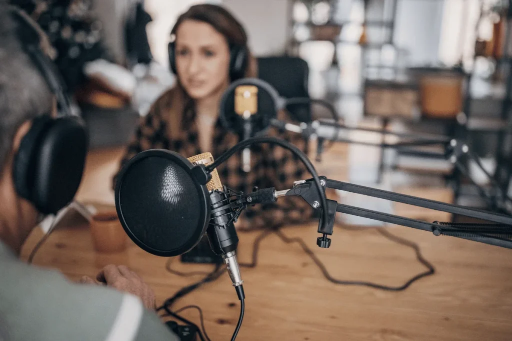 Close-up of a podcast microphone with a blurred view of hosts in the background.