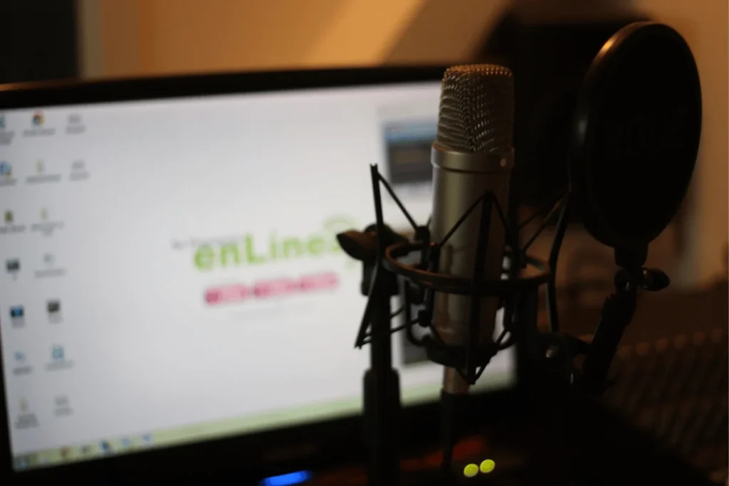 Podcast recording equipment featuring a high-quality microphone and screen filter, blurred monitor behind.