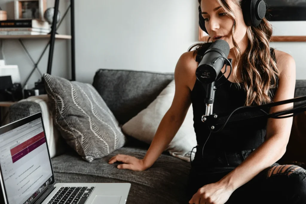 Woman recording a podcast on a couch with a laptop.