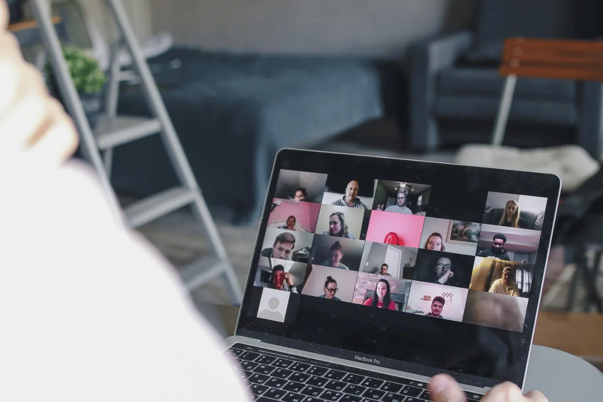 A group video conference on a laptop, displaying multiple participants' faces in a digital grid layout.