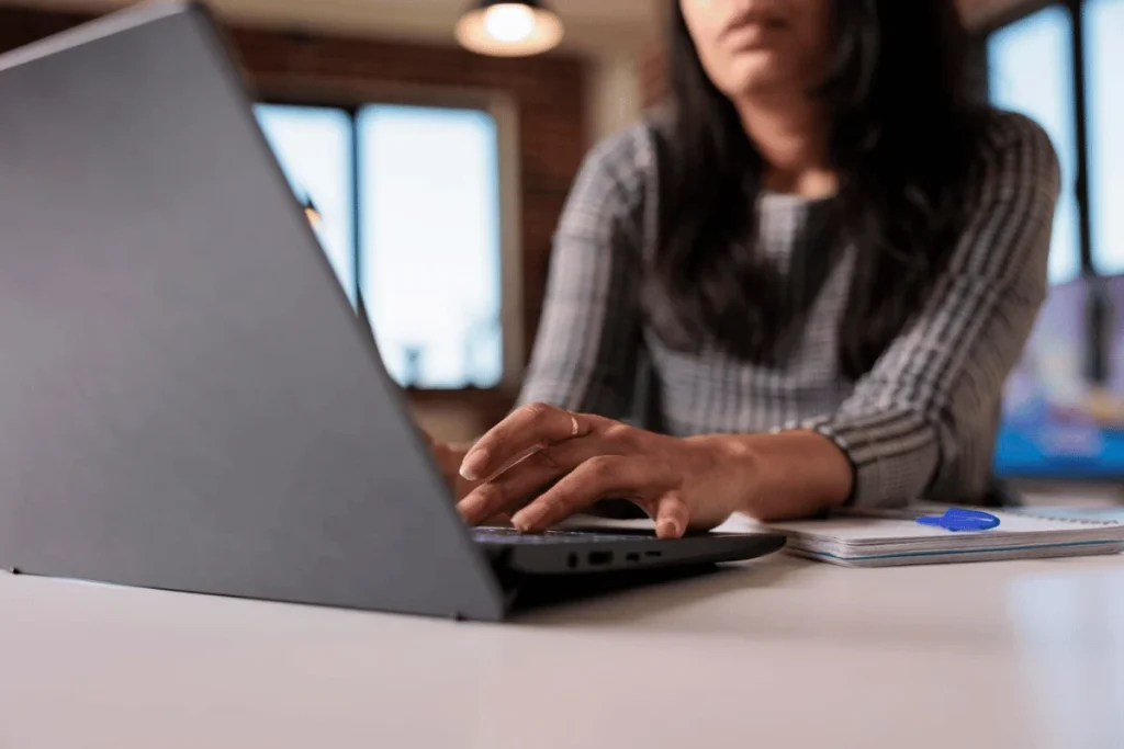 Close-up of a person's hands using a laptop on a well-lit desk.