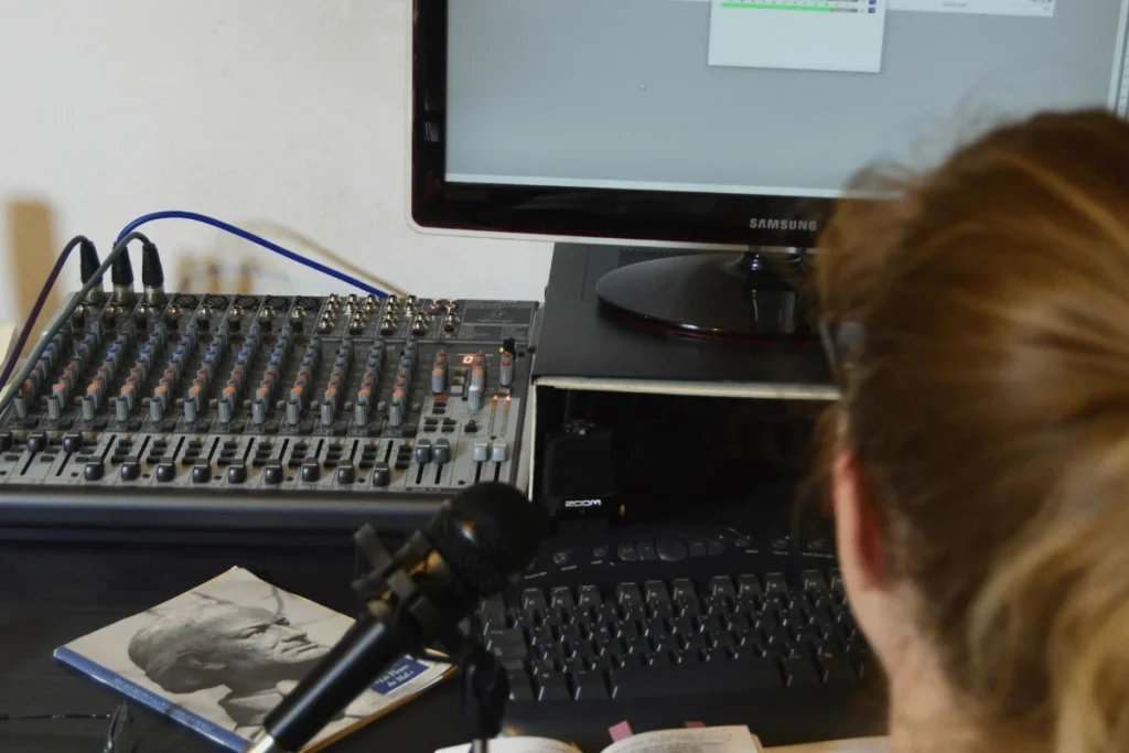 Woman working at audio mixer and desktop setup.