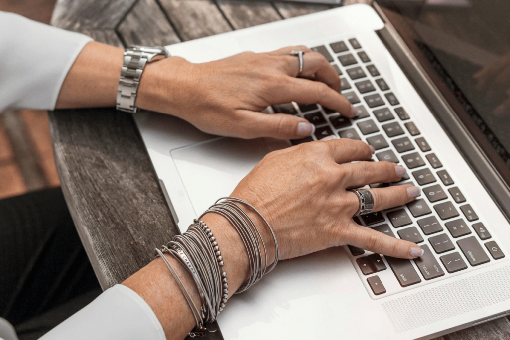 Close-up of hands typing on a chic laptop keyboard with silver bracelets.