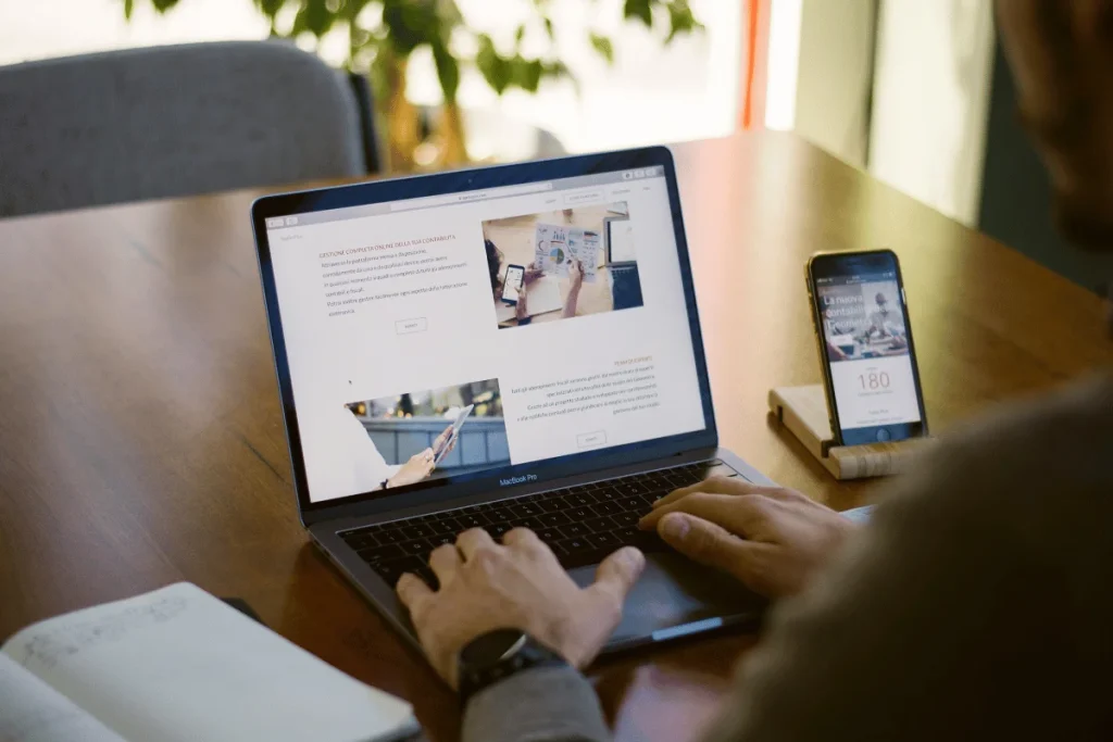 Person working on a MacBook Pro while viewing a website at a wooden desk.