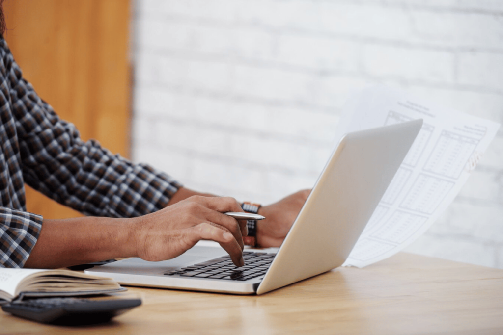 Person in a plaid shirt working on a laptop with financial documents in hand.