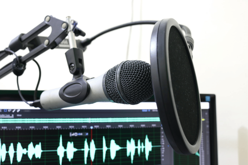 Professional microphone setup with pop filter and sound waveform on the computer screen.