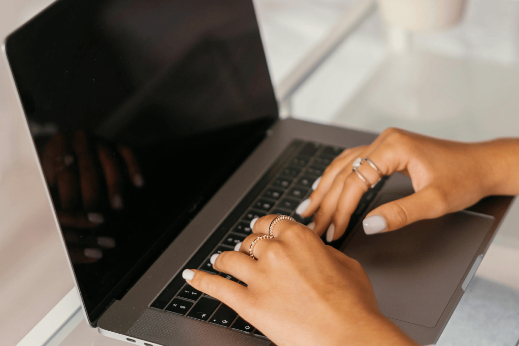 Delicate hands with rings using a modern laptop on a white desk.