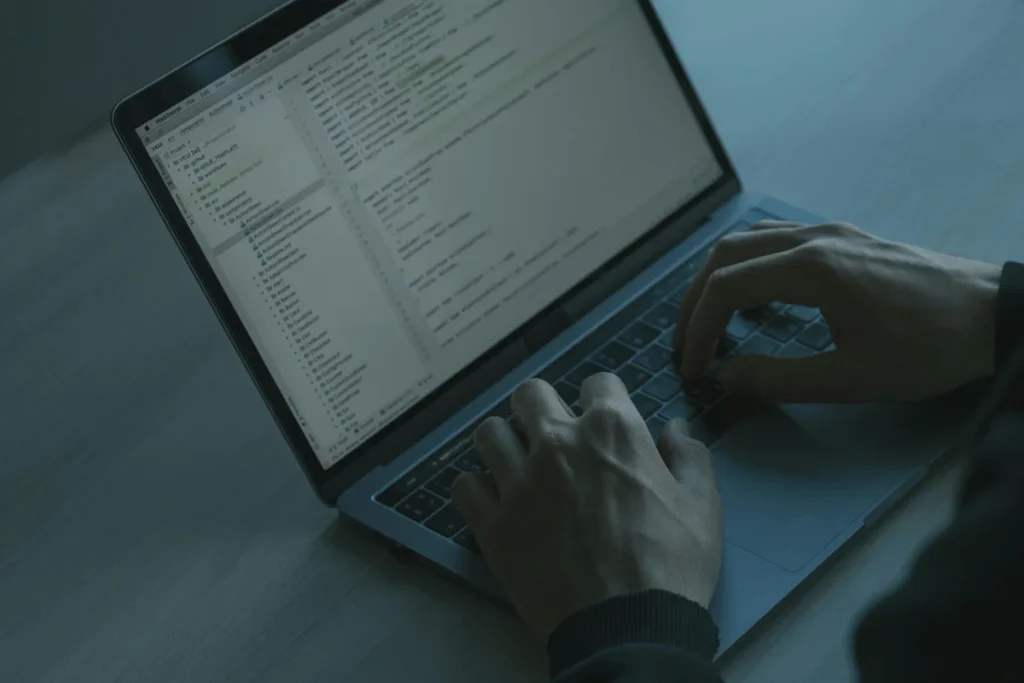 A person coding on a laptop with programming scripts open on the screen.
