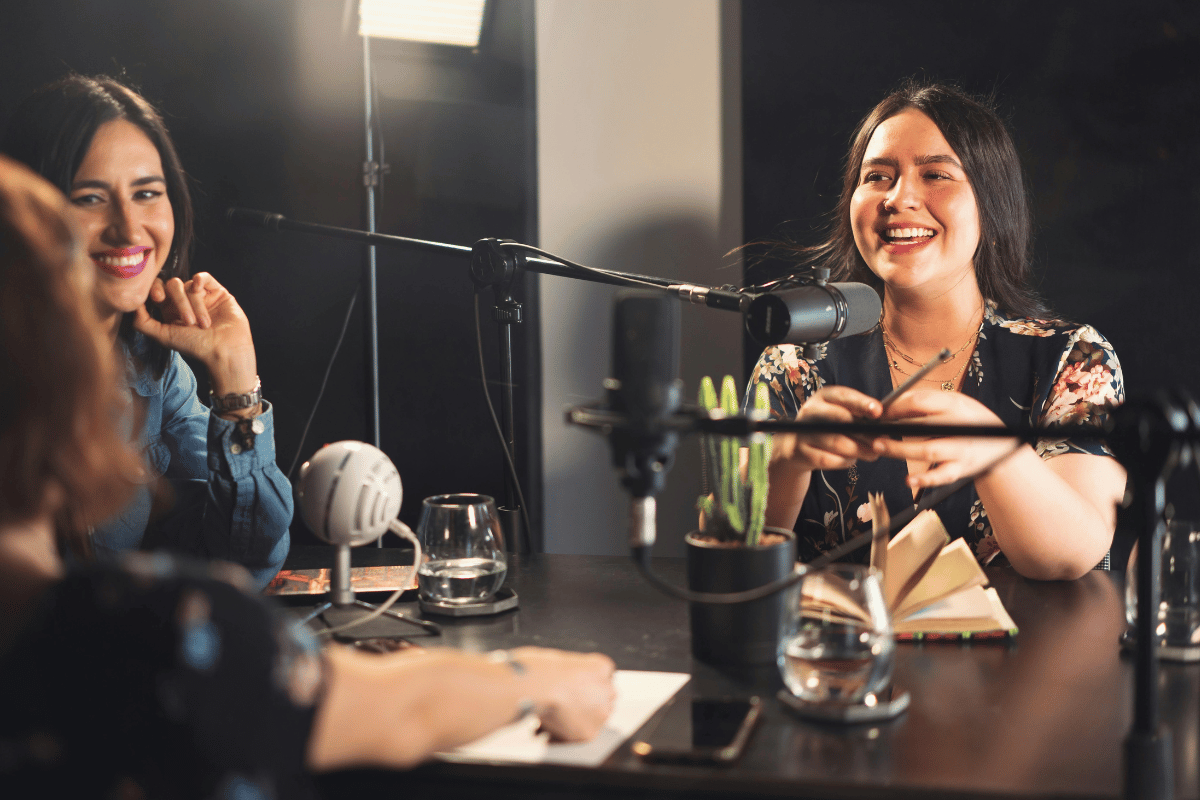 Smiling female podcasters recording an episode with professional mics.