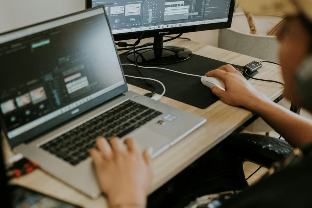 Person video editing on a laptop with dual screens.