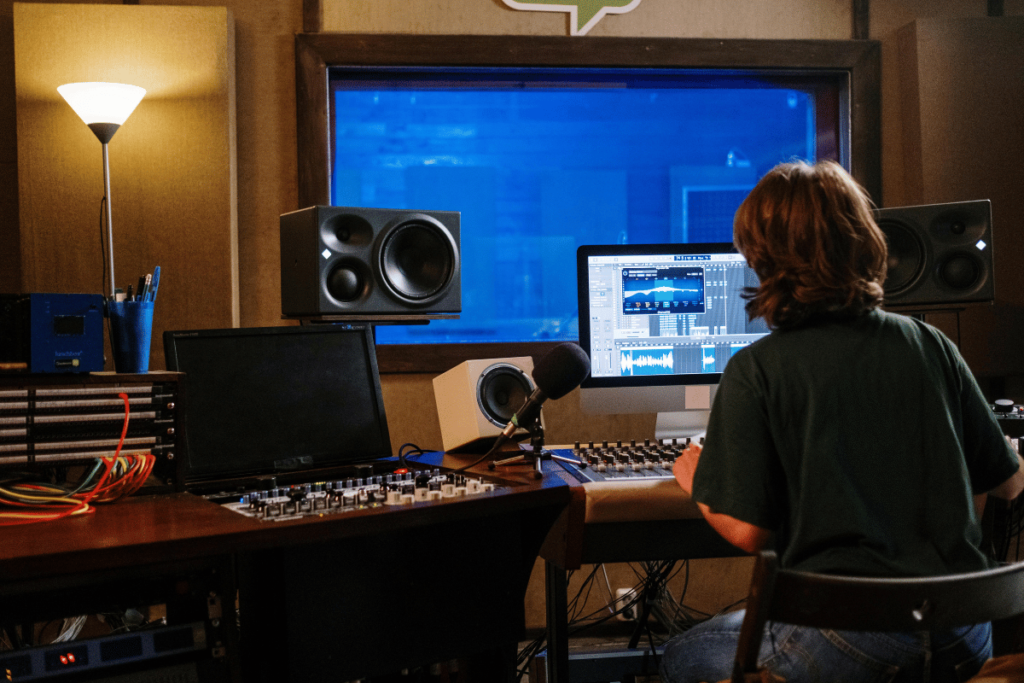 Producer editing audio on a computer with studio monitors in the background.