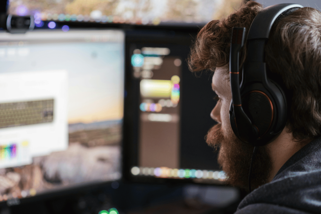 Man with beard using headphones while focused on a computer monitor.