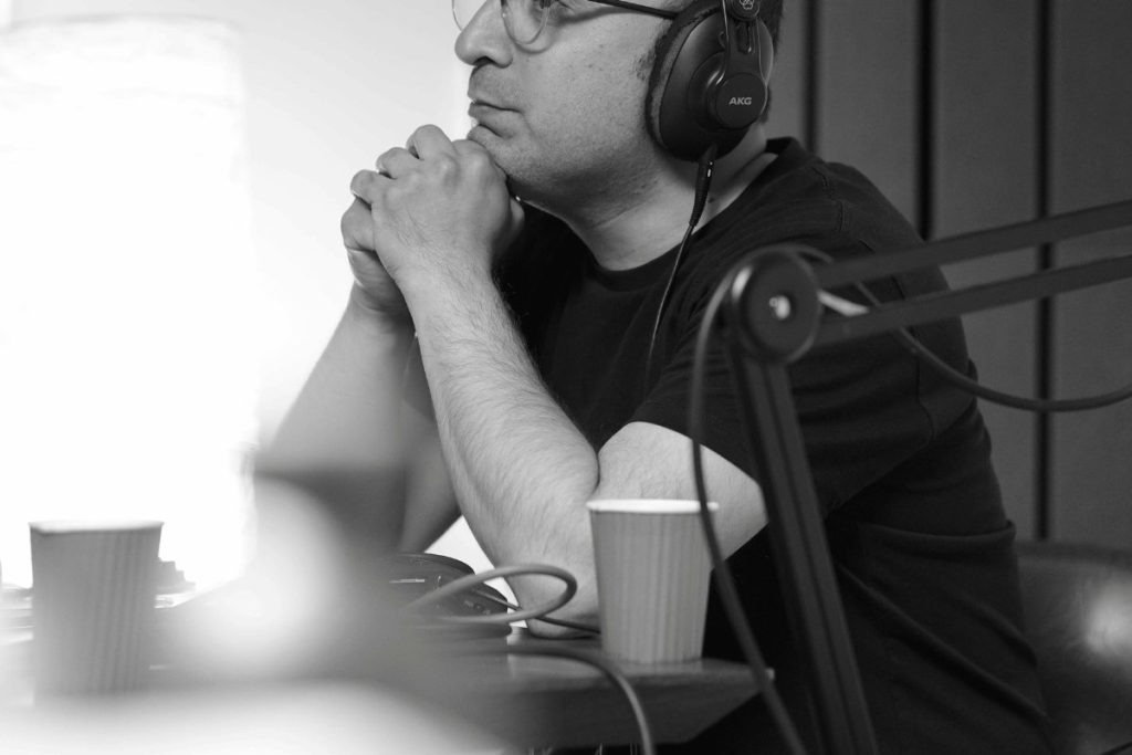 Man in headphones sitting at a podcast desk in a recording studio.