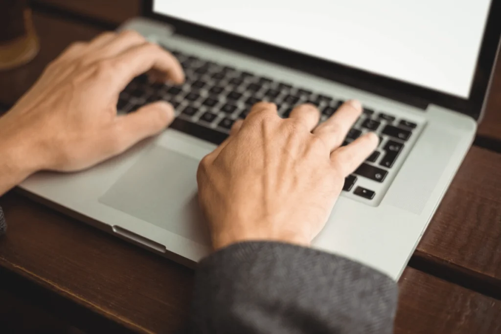 Focused shot of hands typing on a laptop in a warm indoor setting.
