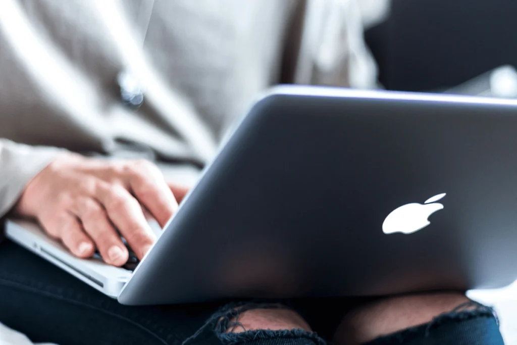 Close-up of hands typing on a MacBook on a user's lap.