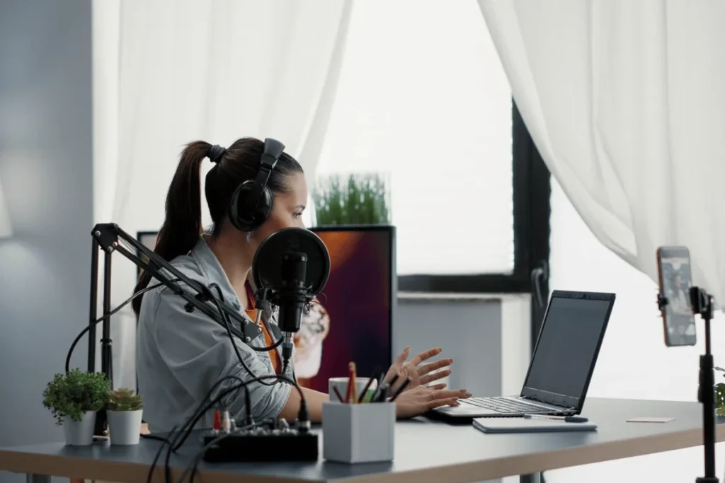 Podcaster speaking into a microphone while using a laptop.