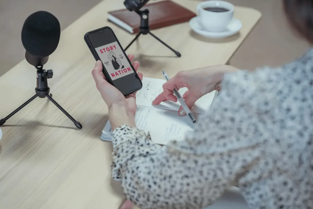 Person taking notes while checking the phone at a podcasting desk.