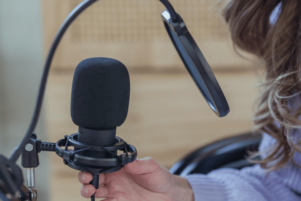 Professional podcast microphone with pop filter being adjusted by a person.