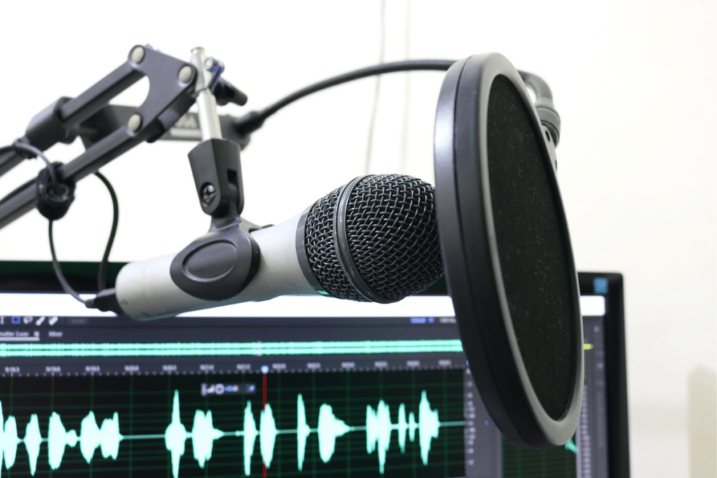 Close-up of studio microphone and pop shield with audio editing software in the background.