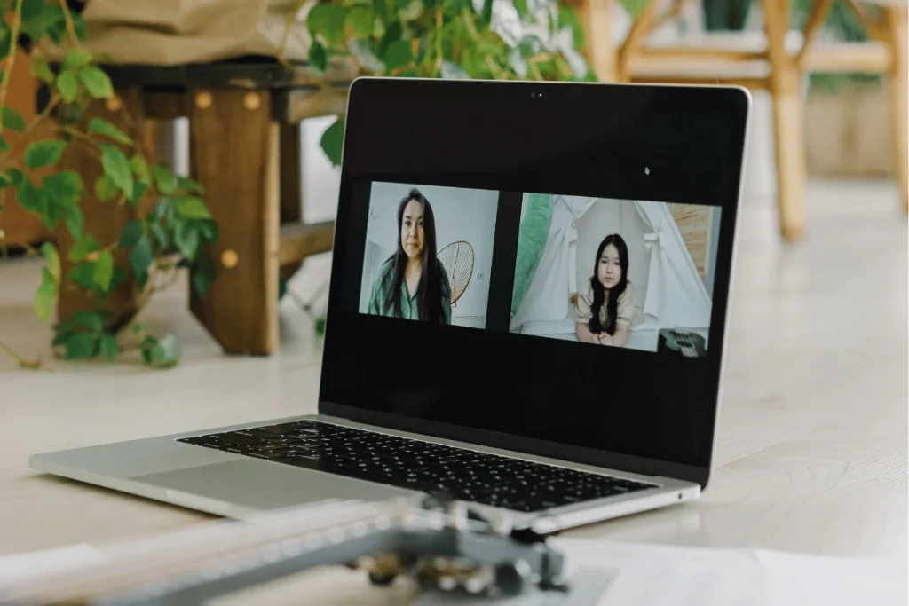 Laptop on a wooden table displaying an online meeting with two Asian women participants.