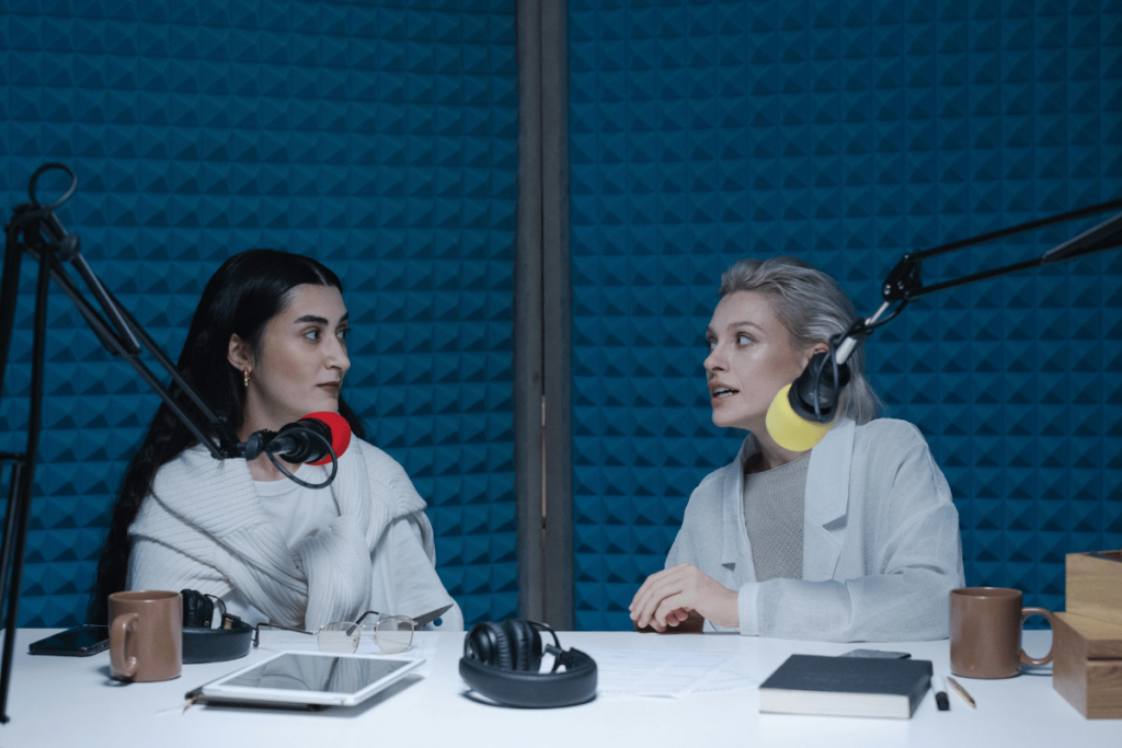 Two women conversing over a microphone in a soundproof podcast studio.