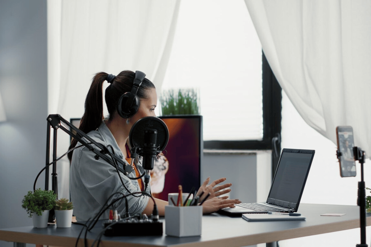 Podcaster recording in a home studio setup with a laptop and microphone.
