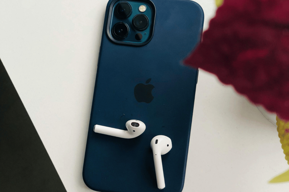Navy blue smartphone with triple camera and white wireless earbuds on a surface.