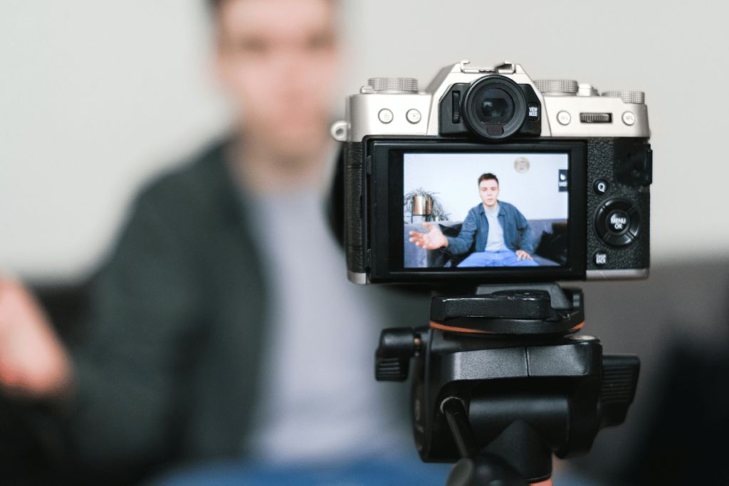 Camera filming a man speaking for a blog with blurred background.