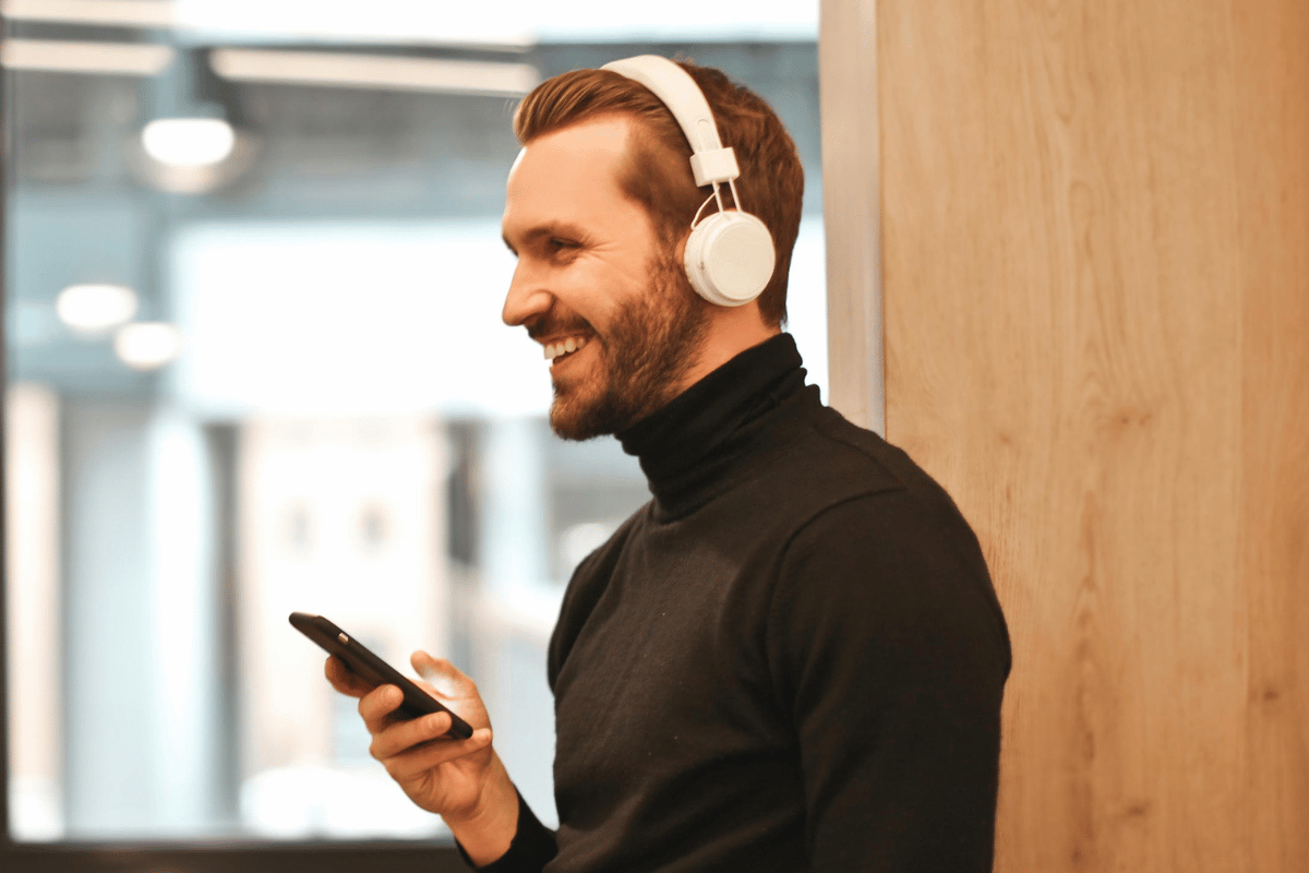 Man in black turtleneck smiling while using smartphone and headphones.