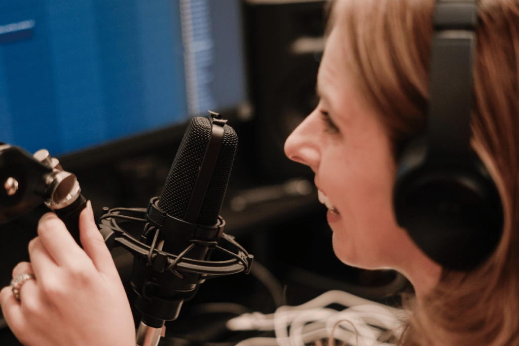 Nora Sudduth with headphones speaking into microphone at audio recording station.