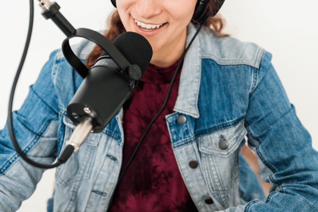 Podcast host with headphones smiling at the mic during a recording session.