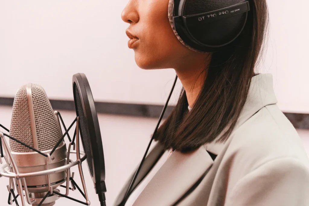 Female podcaster with headphones on, recording audio in a studio with a professional microphone.