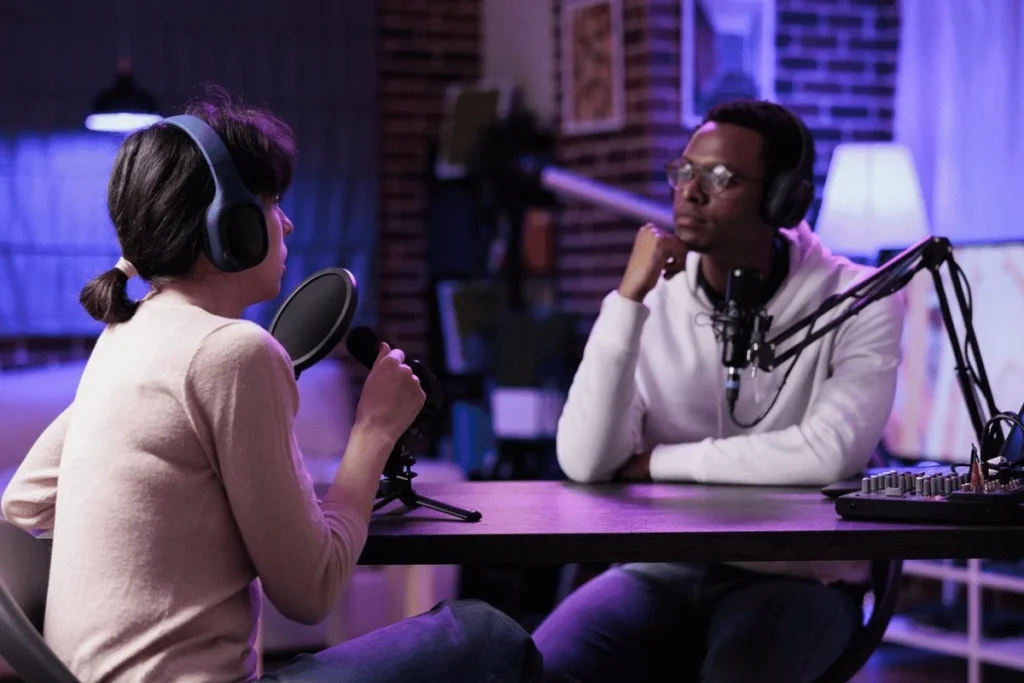 Two podcasters engaged in a conversation in a dimly lit recording studio.