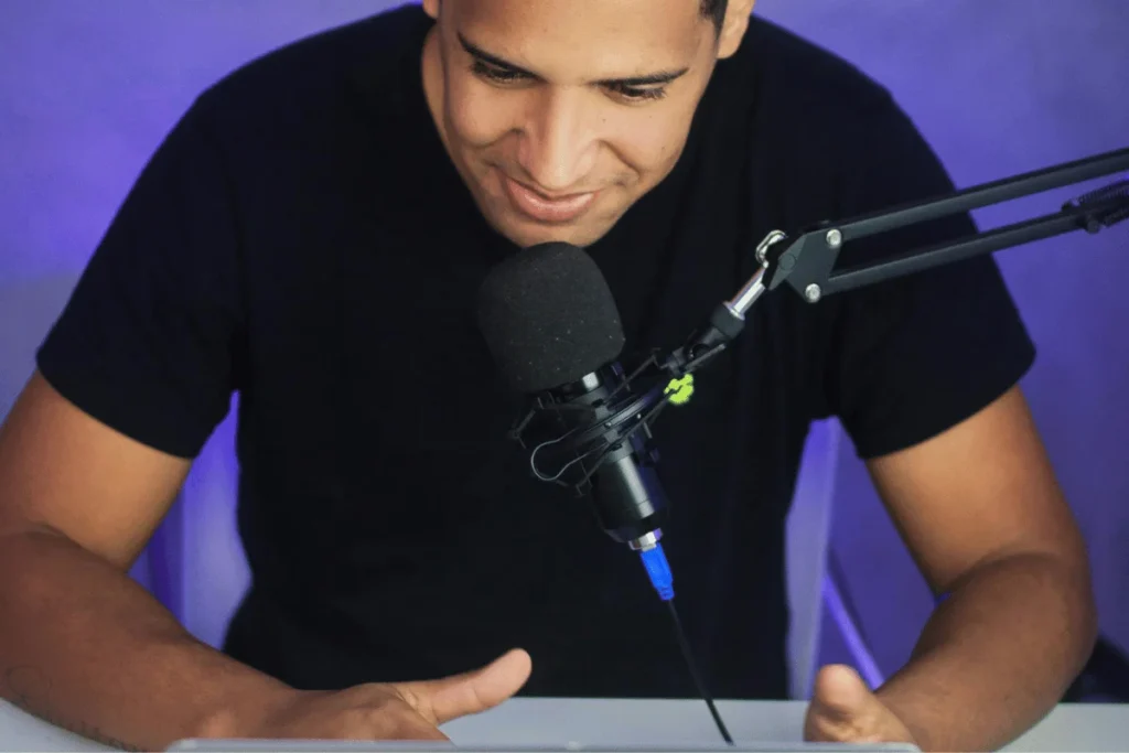 Podcaster speaking into a microphone during a recording session, with a smile on his face.