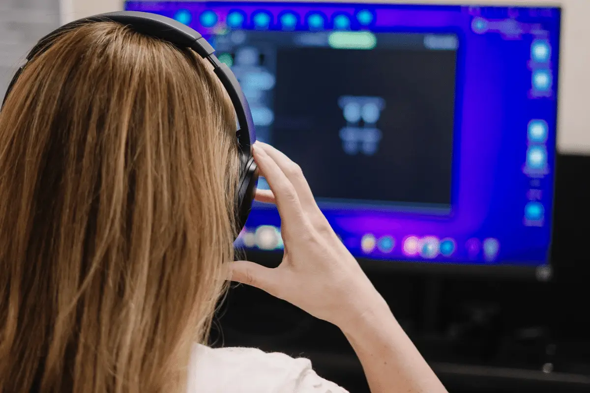Woman with long hair using gaming headset in front of a computer monitor.