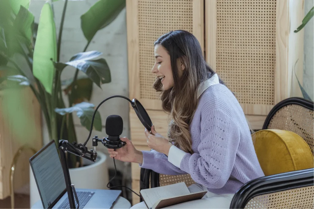Woman recording a podcast at home with a microphone and laptop.