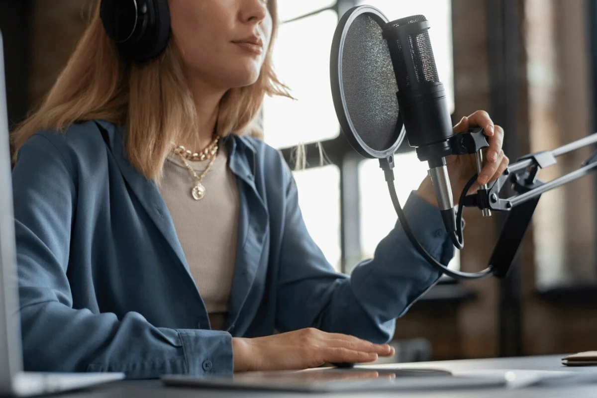 Female podcaster wearing headphones and speaking into a professional microphone with a pop filter.