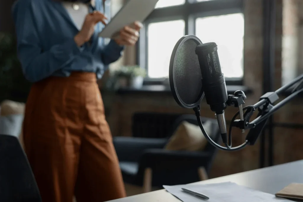 Podcaster standing with notes, professional microphone in focus on a podcast recording setup.