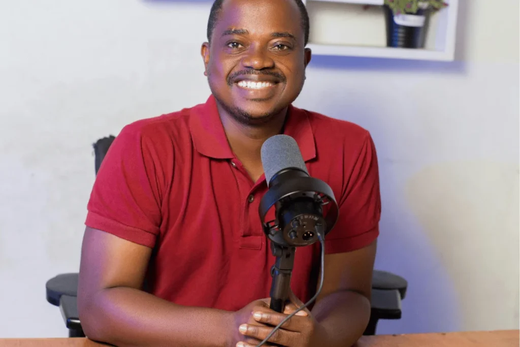 Smiling man in red polo holding a podcast microphone.