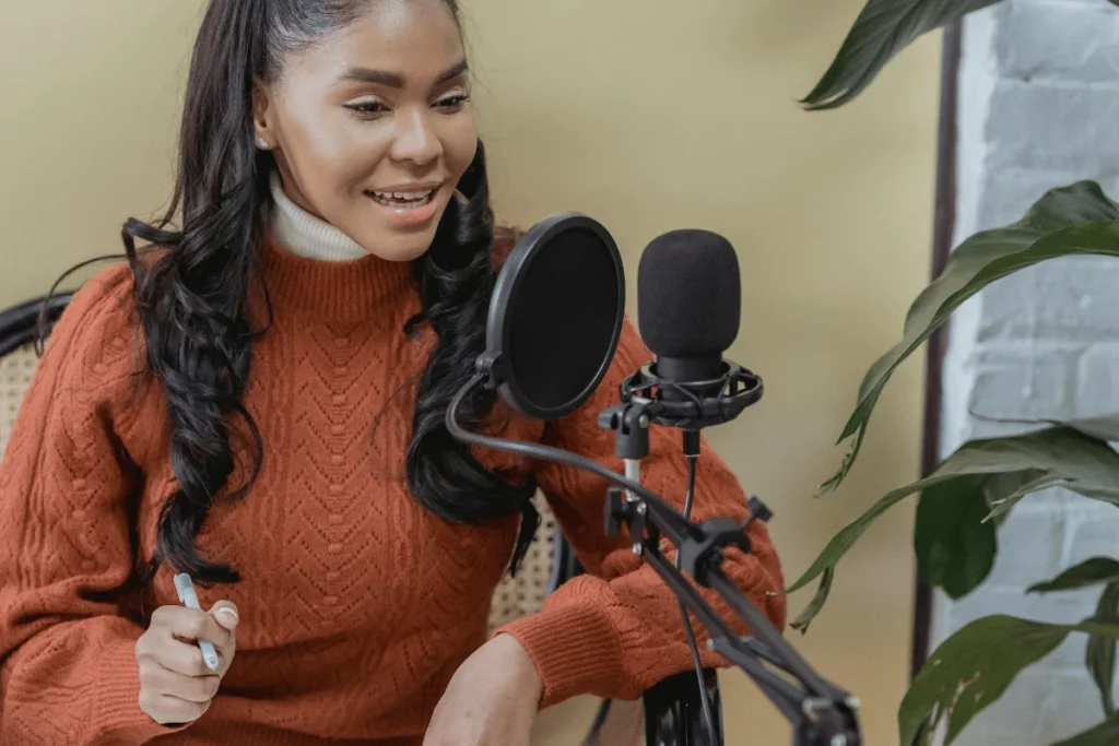 Smiling woman in orange sweater recording with studio microphone and pop filter.