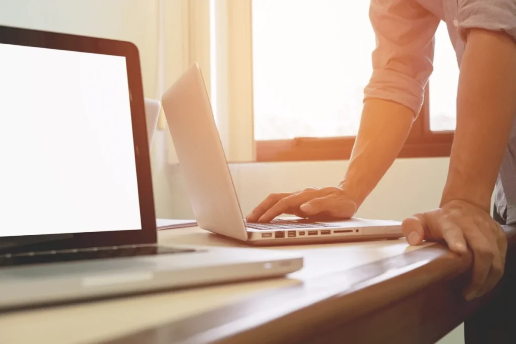 Side view of hands on a laptop keyboard with a sunlit backdrop.