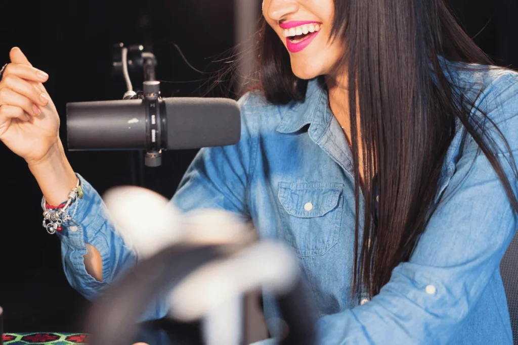 Smiling female podcaster speaking into a studio microphone.