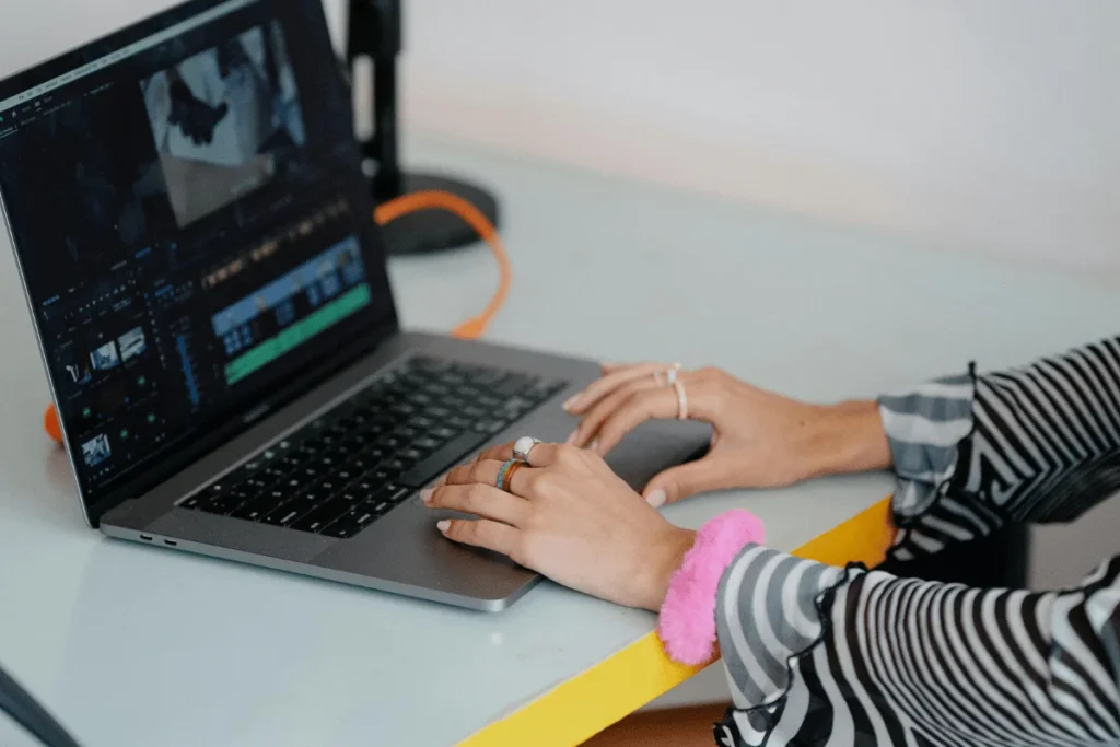 Woman with striped sleeves working on video post-production on a laptop.